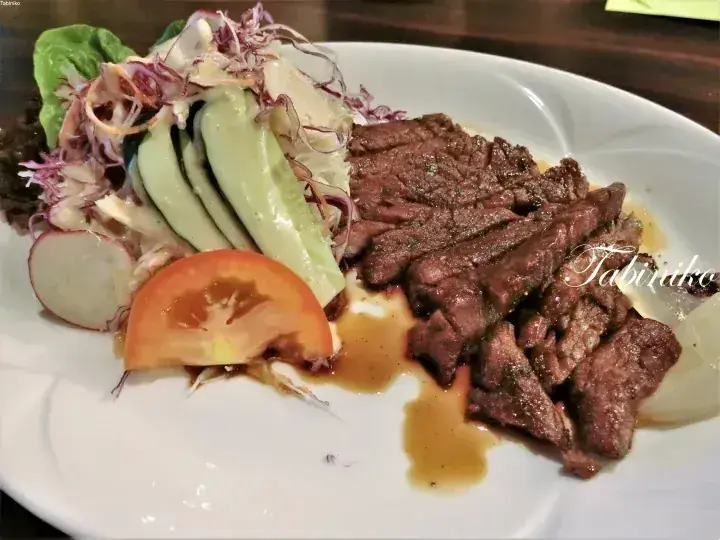Sliced grilled beef steak served with fresh salad including cucumber, tomato, and radish on a white plate.