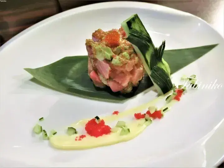 Plated tuna tartare with avocado and roe garnished with cucumber leaves and sauce