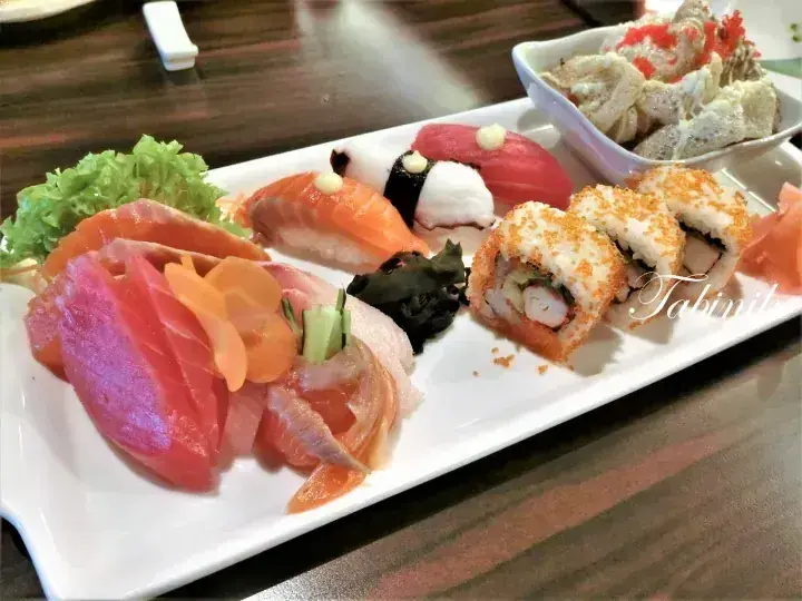 Assorted sushi platter with sashimi, nigiri, and rolls served on a white rectangular plate.