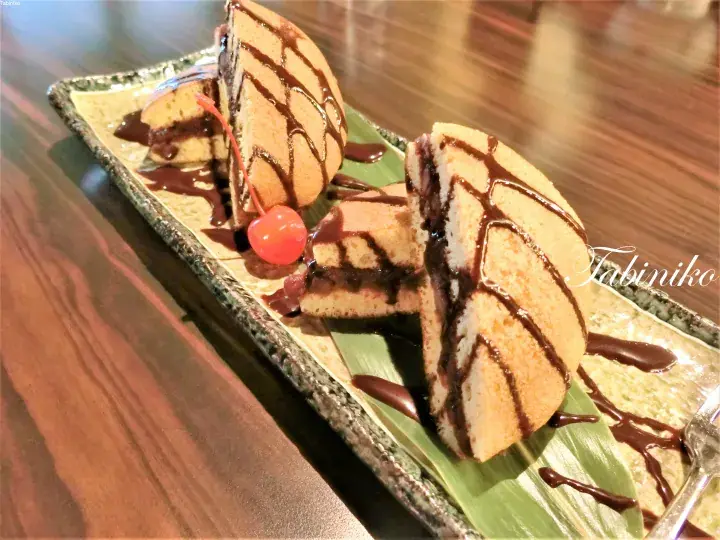 チョコレートソースをかけた生地のスポンジケーキとチェリーが長方形の皿に盛り付けられている。