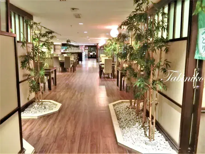 Spacious dining area with wooden floors, bamboo plants in white pebble beds, and modern seating.