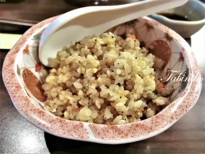 A bowl of fried rice with egg and vegetables in a traditional patterned ceramic bowl with a spoon.