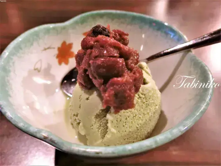 Matcha ice cream topped with red bean paste served in a traditional ceramic bowl with a spoon.