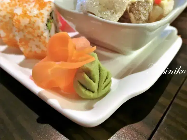 A plate of sushi rolls, pickled ginger, wasabi, and a side dish of fried tofu and meatballs.