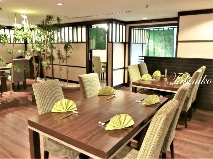 Modern dining room with wooden tables, striped chairs, and green bamboo decor featuring a noren curtain with Japanese text.