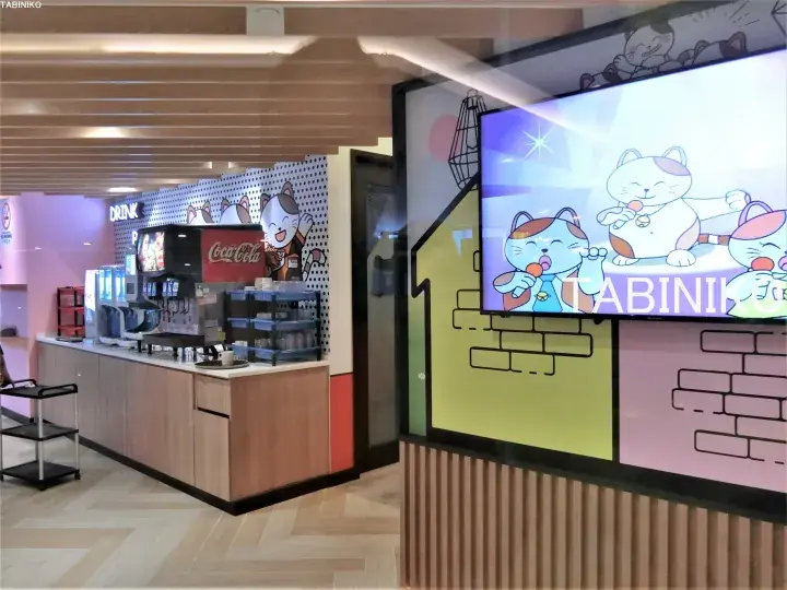 Coca-Cola beverage station and digital screen featuring Labini cat illustrations inside a modern commercial space.