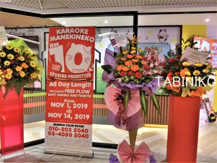 Karaoke Manekineko opening promotion banner displaying RM10 per pax offer with celebratory flower baskets outside the venue.