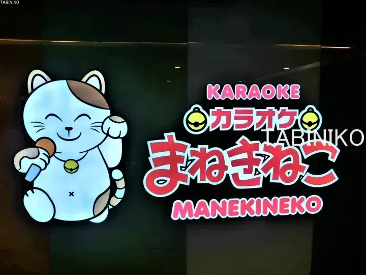 マイクを持つ招き猫のキャラクターが描かれたカラオケまねきねこ看板。