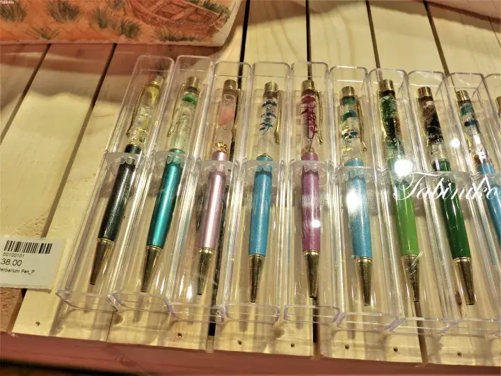 Colorful pens with dried flowers inside displayed in clear plastic packaging on a wooden shelf.