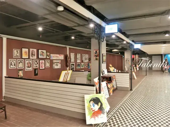 茶色の壁に額装された肖像画が並び、イーゼルには道化師の絵が展示されたギャラリーの内部。