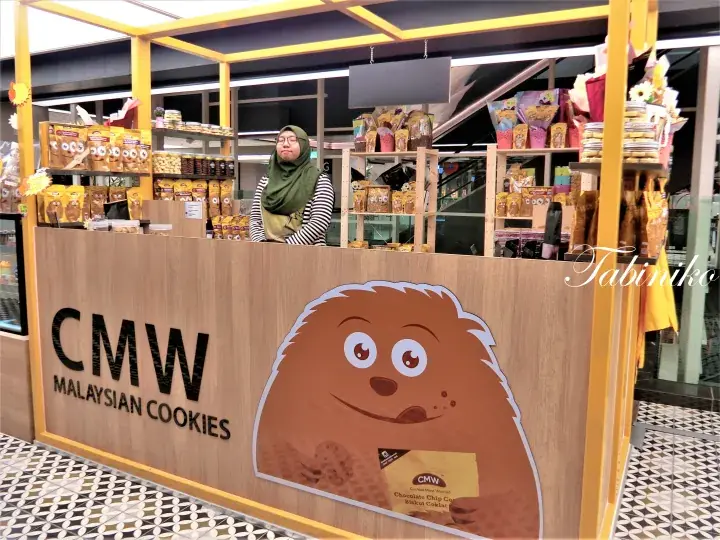 CMW Malaysian Cookies stall with mascot and staff inside a shopping mall.