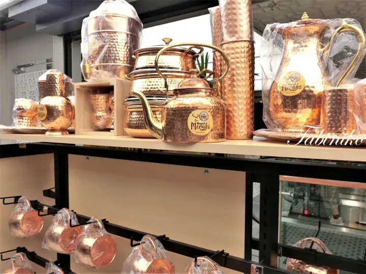 Handcrafted copper tea sets and tumblers displayed on wooden shelves at a Tabiriko store.