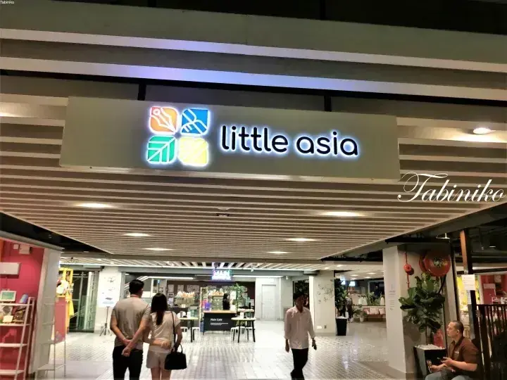 照明が点灯した看板が目立つ「Little Asia」フードコート入口と店内を歩く人々。