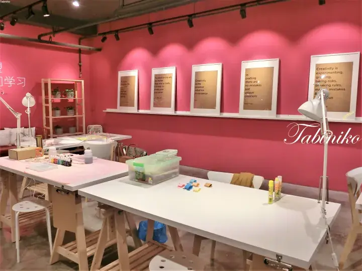 Pink-walled creative studio with white work tables, art supplies, and framed motivational quotes on the wall.