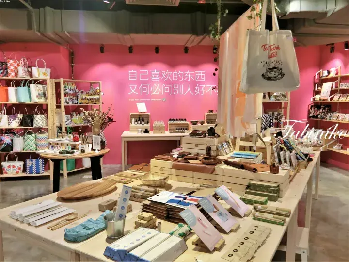 A lifestyle shop interior with pink walls, wooden displays, and stationery items, featuring the Chinese slogan &lsquo;自己喜欢的东西 又何必问别人好不好&rsquo; (Why ask others if you like it yourself).