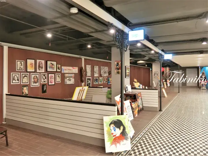 Interior of a gallery space with framed portraits on a brown wall and a clown painting on an easel.