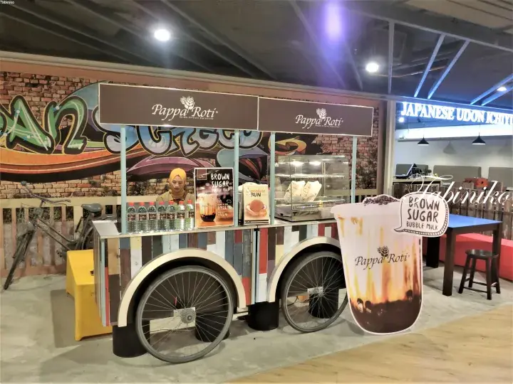 A Pappa Roti food cart featuring Brown Sugar Bubble Milk, displayed at a food court with a Japanese Udon stall in the background.
