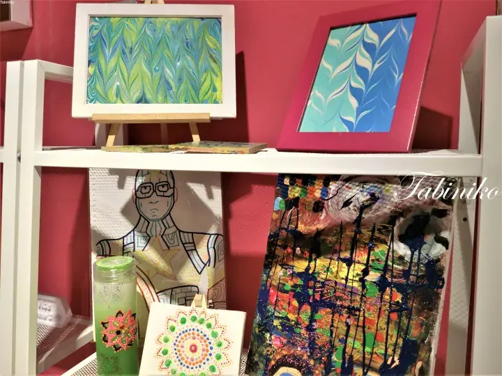 Colorful abstract art and a line drawing displayed on a white shelf against a pink wall.