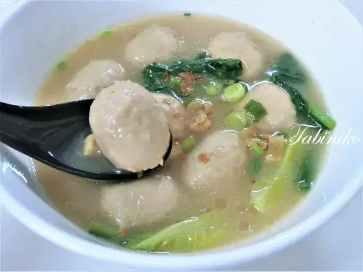 緑の野菜と挽肉が入った透き通るスープから、黒いスプーンで魚肉団子を持ち上げている様子。