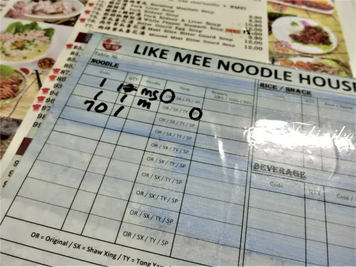 A close-up of a Like Mee Noodle House order slip with handwritten noodle selections and pricing details.