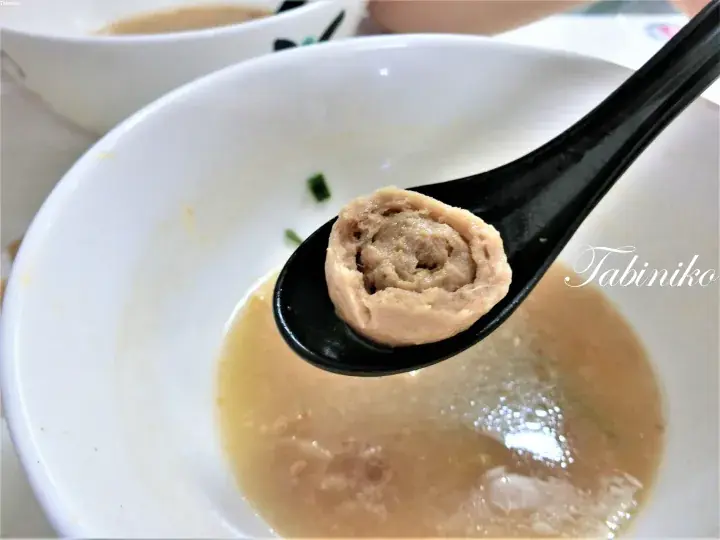 A close-up of a pork ball soup with a spoon lifting a cross-section of the meatball from a white bowl.