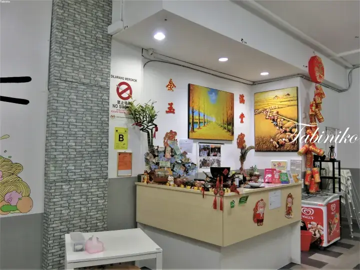 Reception counter with gold accents and artwork at a Malaysian property, featuring a no smoking sign and decorative items.