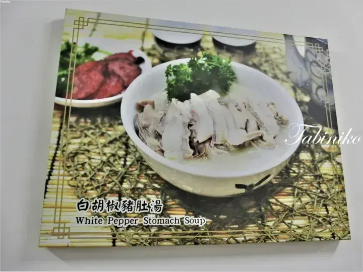 パセリを添えた白胡椒豚肚湯のボウルと、背景に見える焼き肉の盛り合わせ。