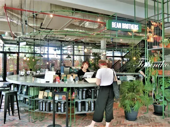 緑とインダストリアルな装飾に囲まれたBean Brothersカフェのカウンターで注文する顧客