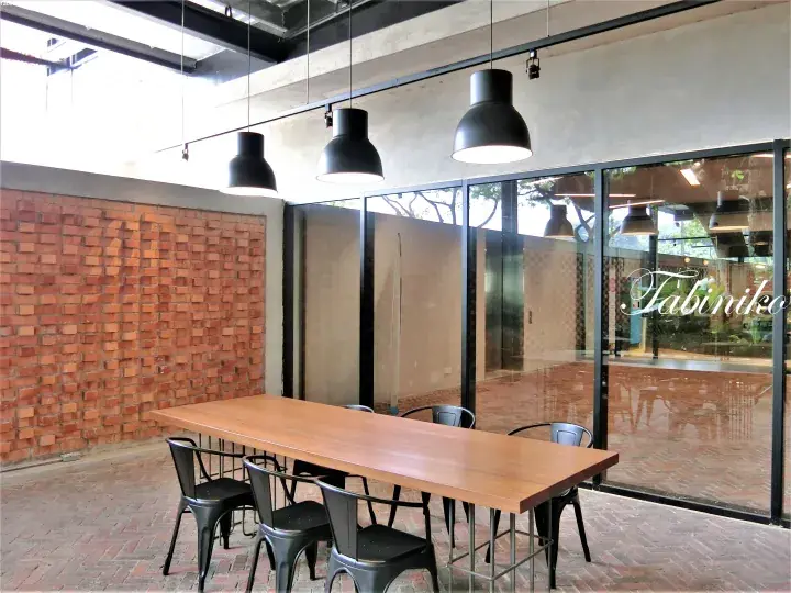 Modern dining area with wooden table, black chairs, brick wall, and glass partition featuring Tabiniko logo