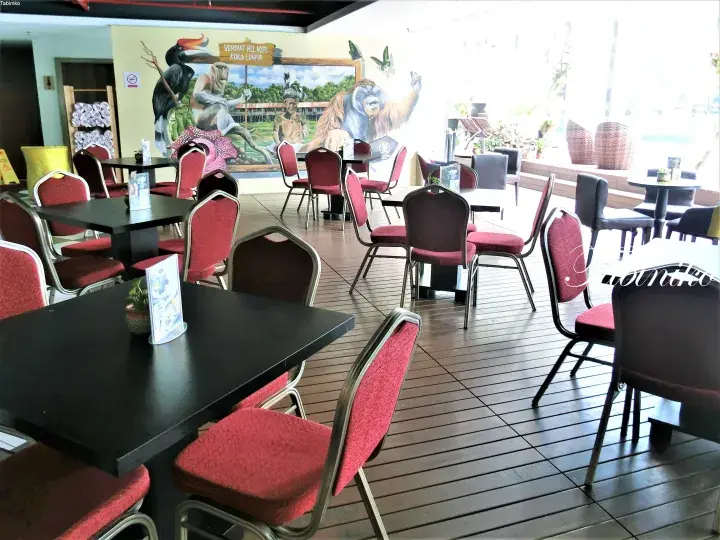 Dining area with red chairs and murals of Malaysian wildlife at a restaurant in Kuala Lumpur.