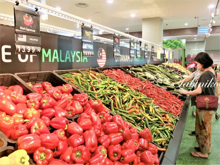 Fresh red capsicum and vegetables displayed at a Malaysia supermarket section with signage.