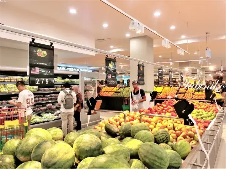 スイカやリンゴが並ぶAEONビッグの鮮魚・野菜売り場で買い物客が品定めをする様子。