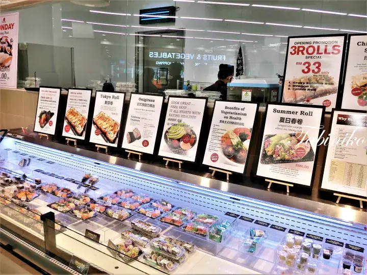 A refrigerated display case filled with various sushi rolls and bento boxes, with promotional signs for Tokyo Roll and Summer Roll visible.