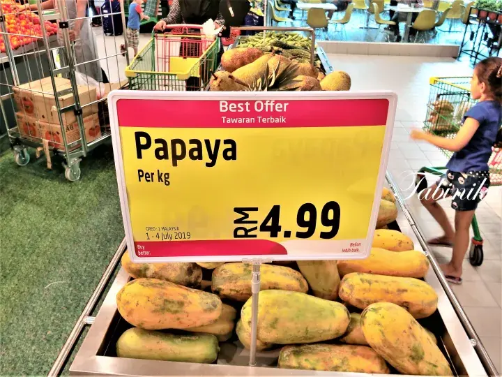 A price sign for papaya at RM4.99 per kg displayed on a supermarket shelf with fresh papayas.