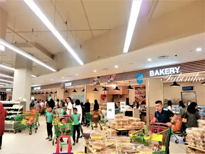 マレーシアの賑やかなスーパーマーケットで、SUSHIやBAKERYの看板が見えるパン売り場を客が買い物している様子。