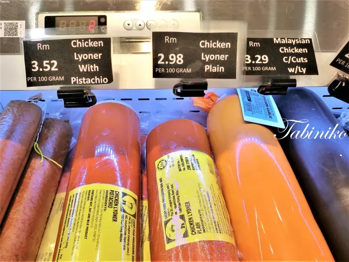 Assorted chicken lyoner sausages with price tags displayed on a refrigerated shelf at a Malaysian market.