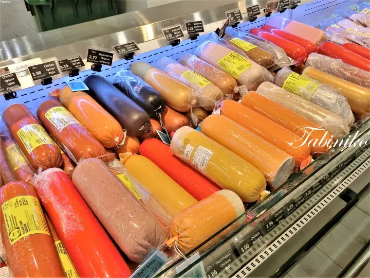 Colorful sausages displayed in a refrigerated supermarket section with price tags.