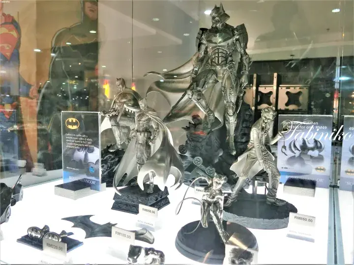 Silver Batman statues and collectibles displayed in a shop window with price tags.