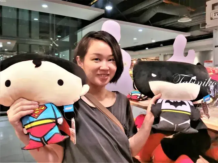 スーパーマンとバットマンのぬいぐるみを持った笑顔の女性。