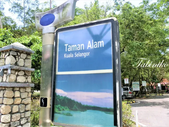 Entrance gate of Taman Alam Kuala Selangor with a large metal sign arching over the driveway surrounded by lush green trees.