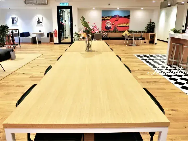 カラフルなアートが飾られたモダンなオープンプランオフィスに設置された、黒い椅子を備えた長い木製ダイニングテーブル。