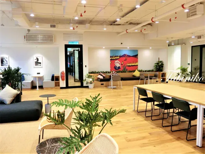 Modern co-working space with wooden floors, a long table, lounge seating, and vibrant wall art.