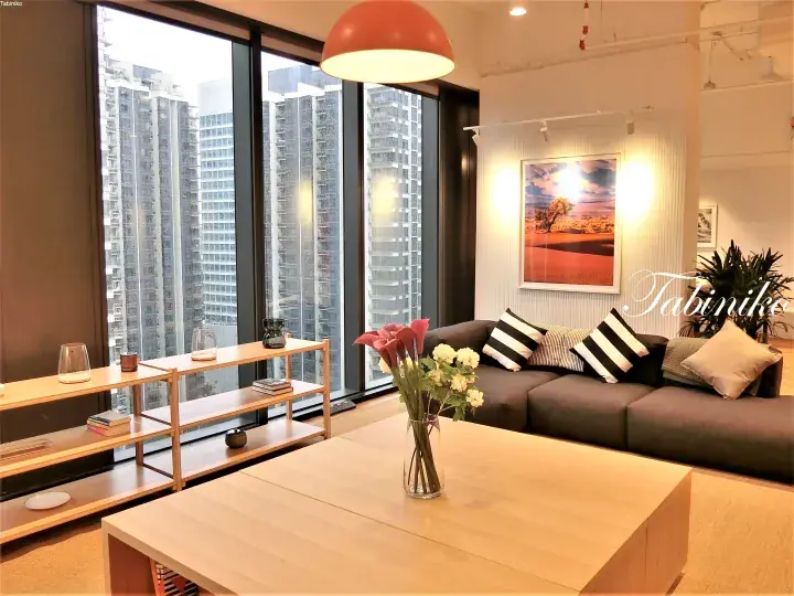Modern living room with grey sofa, wooden coffee table, and large windows overlooking high-rise buildings in Kuala Lumpur.