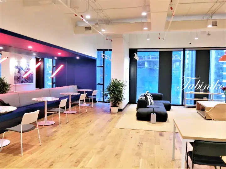 Modern co-working space interior with wooden floors, blue lounge seating, and large windows at a Tabinika location