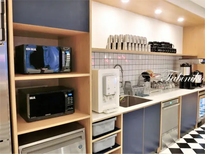 Kitchenette with halal and non-halal microwaves, water dispenser, and coffee station in a modern property.