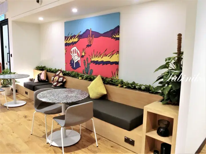 Cozy lounge area with a built-in wooden bench, grey cushions, and a vibrant desert-themed painting on the wall.