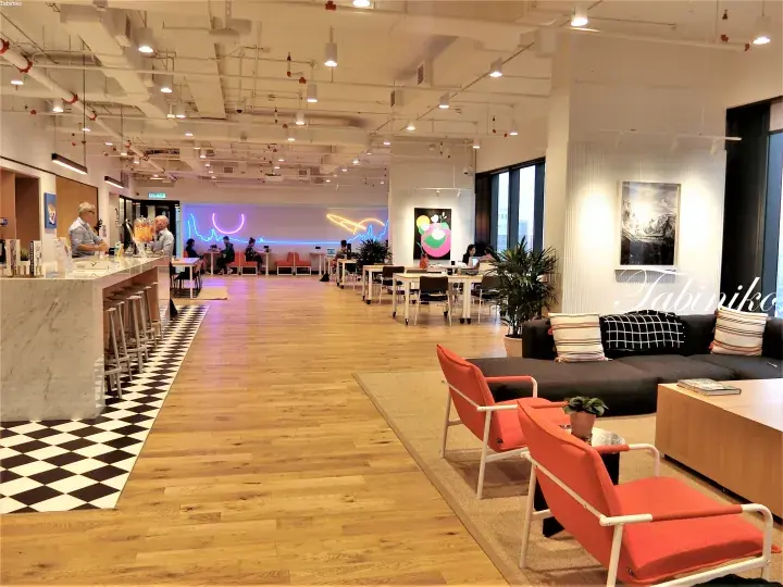 Modern co-working space with wooden floors, orange chairs, and a neon art wall.