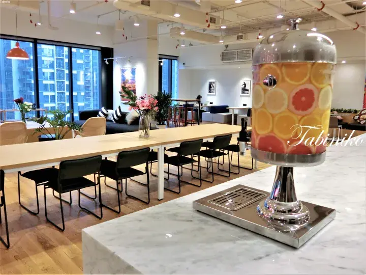 Modern office lounge with a fruit-infused water dispenser on a marble counter and a long communal table.