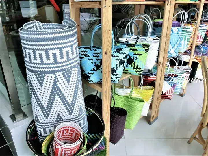 マレーシアの店舗で木製棚に並べられたカラフルな籐バッグとロール状のマット。