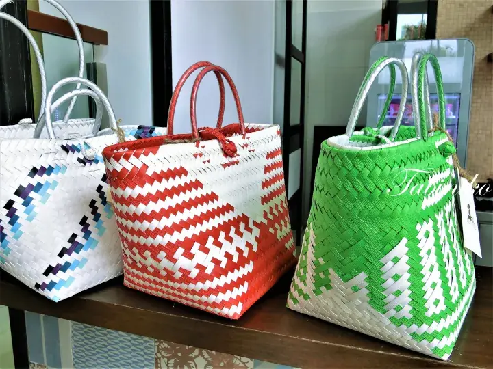 Colorful woven rattan bags with geometric patterns displayed on a wooden shelf.